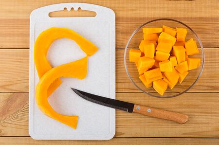 Cubes of cut ripe pumpkin in plate, cutting board and knife on wooden table. Top viewの写真素材