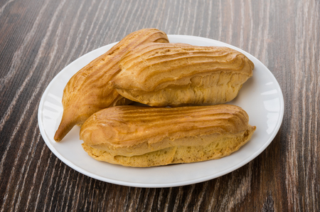 Eclairs in white plate on dark wooden table