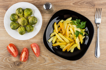 Fried potatoes in plate, brussels sprouts, pepper, tomatoes and fork on wooden table. Top viewの写真素材