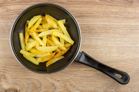 Pieces of fried potatoes in frying pan on wooden table. Top viewの写真素材