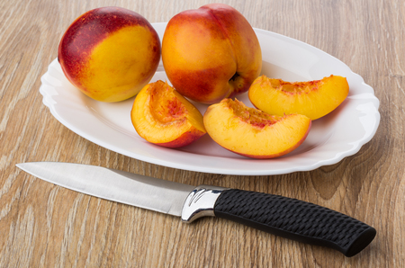Pieces of nectarines in white dish and kitchen knife on wooden tableの写真素材