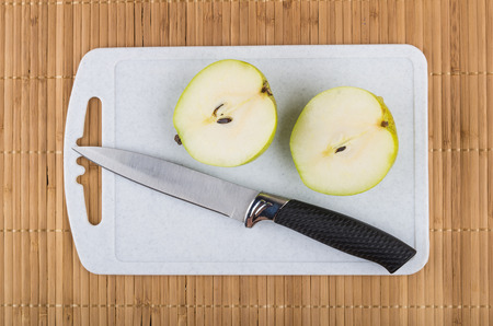 Two half of pear and knife on cutting board on bamboo mat. Top viewの写真素材