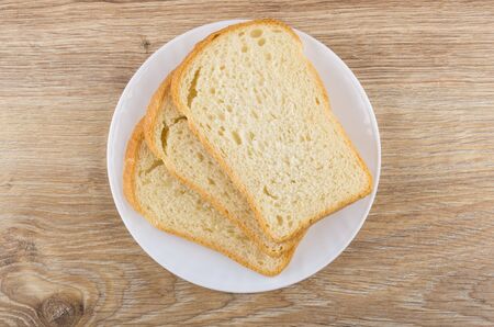 Pieces of white bread in glass plate on wooden table. Top view