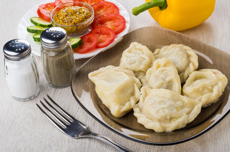 Boiled dumplings in plate, mustard and vegetable, salt, pepper and fork on wooden tableの写真素材