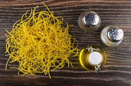 Heap of thin noodles, bottle of vegetable oil, salt and pepper on wooden table. Top view