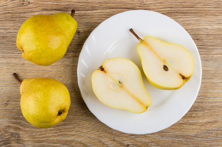Yellow pears and halves of pear in plate on wooden table. Top viewの写真素材
