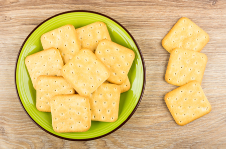 Heap of crackers in green plate and on wooden table. Top viewの写真素材