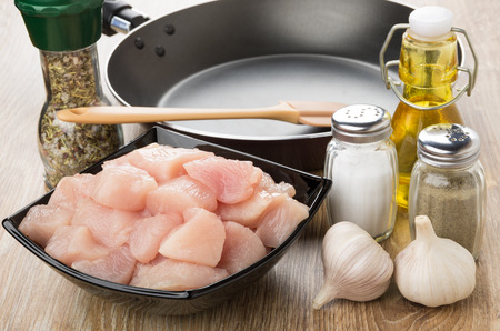 Pieces of raw chicken meat in bowl, frying pan, vegetable oil and condiments on wooden tableの写真素材