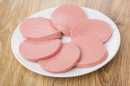White plate with slices of boiled sausage on wooden tableの写真素材