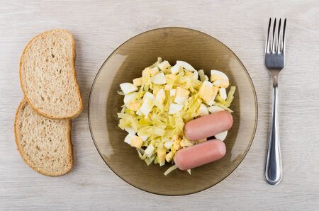 Fried cabbage with sausages in plate, bread and fork on wooden table. Top viewの写真素材