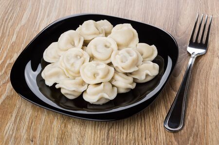 Black plate with boiled dumpling and fork on wooden tableの写真素材
