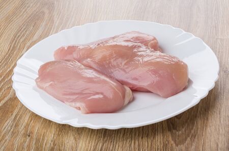 Pieces of raw chicken breast in white plate on wooden tableの写真素材