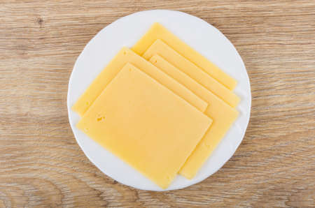 Slices of cheese in white plate on wooden table. Top view