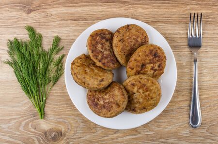 Fried cutlets in white plate, bunch of dill and fork on wooden table. Top viewの写真素材