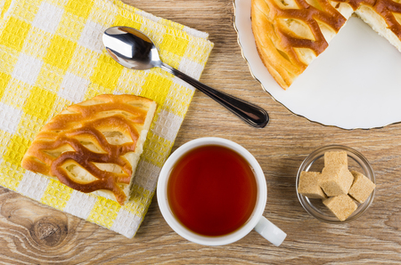 Piece of pie with cottage cheese, teaspoon on napkin, tea, sugar in bowl on wooden table. Top viewの写真素材