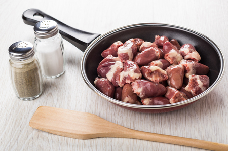 Raw chicken hearts in frying pan, salt, pepper, spatula on wooden tableの写真素材