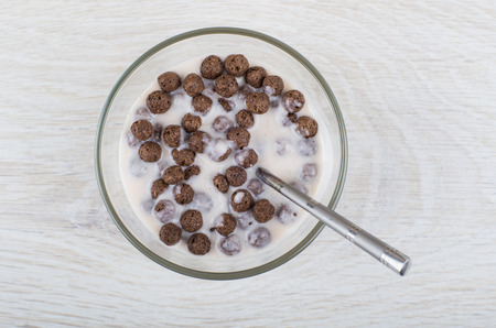 Chocolate corn balls with yogurt in transparent bowl and teaspoon on wooden table. Top view