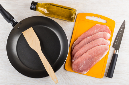 Raw pork schnitzel on cutting board, vegetable oil, frying pan, spatula and kitchen knife on wooden table. Top viewの写真素材