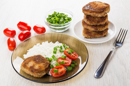 Fried cutlets with rice, tomatoes, green onion in plate, stack of cutlets in saucer and fork on...