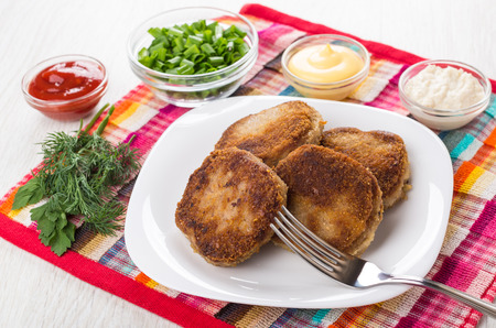 Fried cutlets in plate, bowls with chopped onion, mayonnaise, ketchup, horseradish, greens on napkin...
