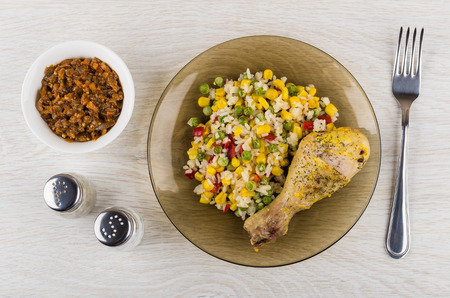 Fried chicken leg with vegetable mix in plate, eggplant caviar, salt, pepper and fork on wooden table. Top viewの写真素材