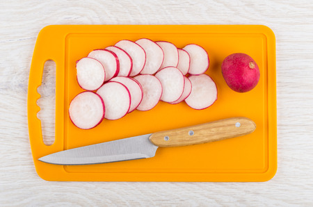 Slices of radishes and kitchen knife on orange cutting board on wooden table. Top viewの写真素材