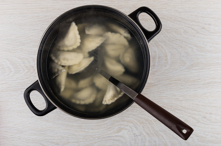 Pan with boiled dumplings and skimmer on wooden table. Top viewの写真素材