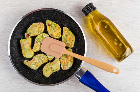 Frozen vegetable nuggets in frying pan, spatula, bottle of vegetable oil on wooden table. Top viewの写真素材