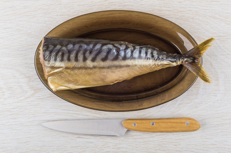 Smoked mackerel in brown dish and kitchen knife on wooden table. Top viewの写真素材