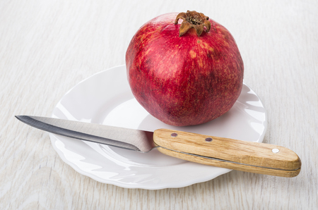 One pomegranate and kitchen knife in white glass plate on wooden tableの写真素材