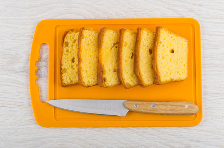 Slices of biscuit, kitchen knife on plastic cutting board on wooden table. Top view