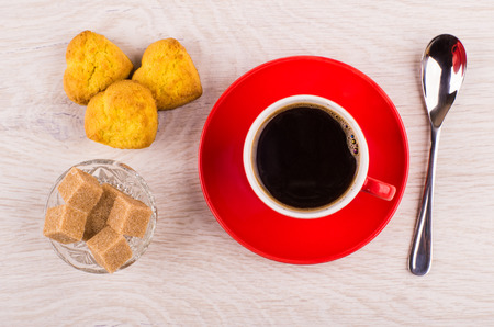 Black coffee in red cup on saucer, spoon, cookies and sugar in bowl on wooden table. Top viewの写真素材