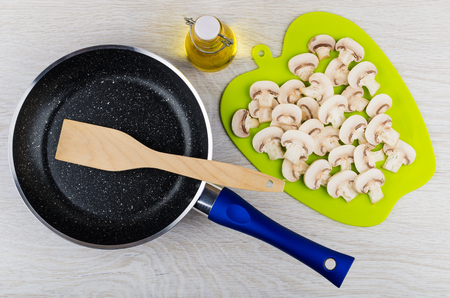 Slices of mushrooms on cutting board, fying pan, spatula, bottle of vegetable oil on wooden table. Top viewの写真素材