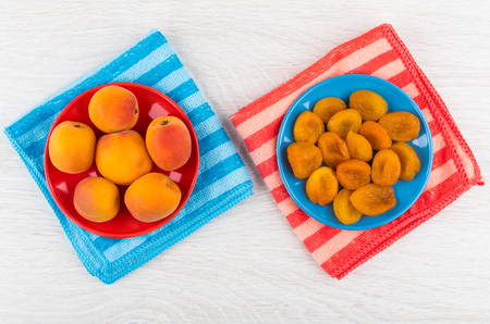Fresh apricots in red saucer, dried apricots in blue saucer on folded napkins on wooden table. Top viewの写真素材
