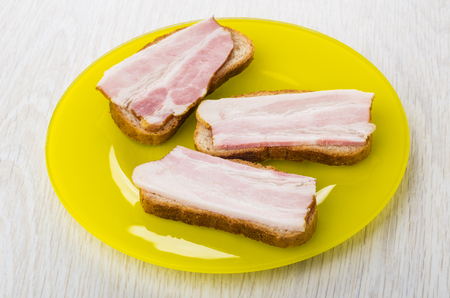 Three sandwiches with bacon in yellow plate on wooden tableの写真素材