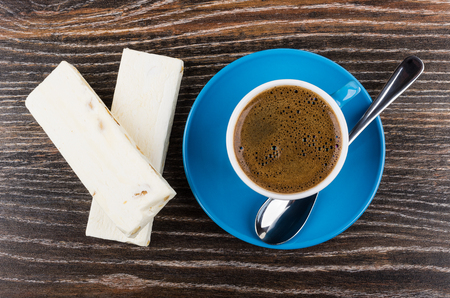 Two nougats, coffee in blue cup, spoon on saucer on wooden table. Top viewの写真素材