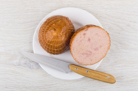 Pieces of round chicken smoked sausage, kitchen knife in plate on wooden table. Top viewの写真素材