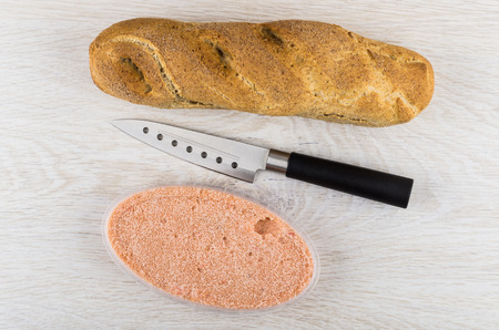 Loaf of bread, kitchen knife, herring caviar with mayonnaise in plastic jar on wooden table. Top viewの写真素材