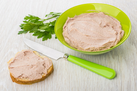 Liver pate in green bowl, parsley, sandwich with liver pate, knife on wooden tableの写真素材