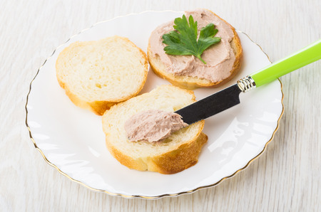 Sandwiches with liver pate and parsley, knife in glass plate on wooden tableの写真素材