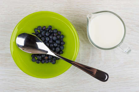 Raw blueberry, spoon in green bowl, jug of milk on wooden table. Top viewの写真素材