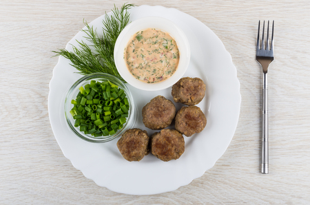 White dish with chicken fried meatballs, dill, bowls with sauce, chopped scallion and fork on wooden table. Top viewの写真素材