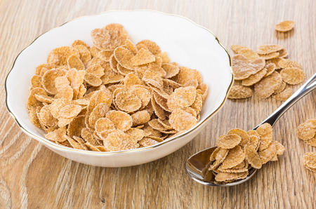 Multi cereal flakes in bowl, spoon with flakes, on wooden table