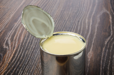 Opened metallic jar with sweet condensed milk on dark wooden tableの写真素材
