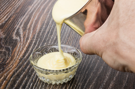 Pouring sweet condensed milk from metallic jar in transparent bowlの写真素材