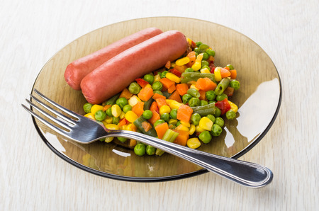 Plate with boiled sausages and vegetable mix, fork on wooden tableの写真素材