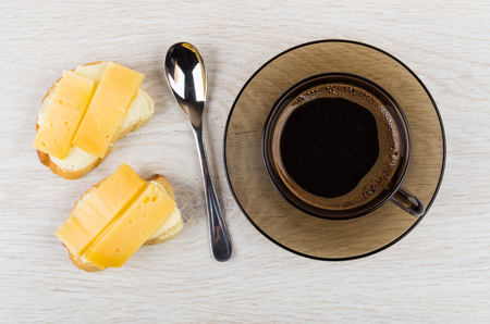 Sandwiches with cheese, cup of coffee on saucer, spoon on wooden table. Top viewの写真素材