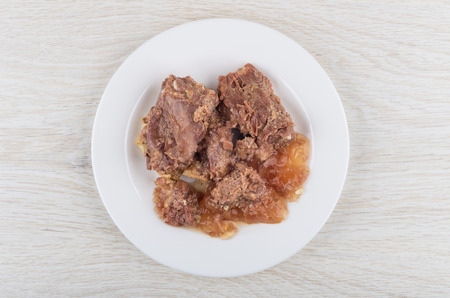 Canned stew beef in white plate on wooden table. Top view