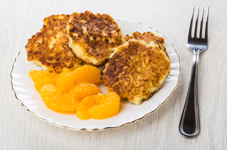 Cottage cheese pancakes and slices of tangerines in white plate, fork on on wooden tableの写真素材