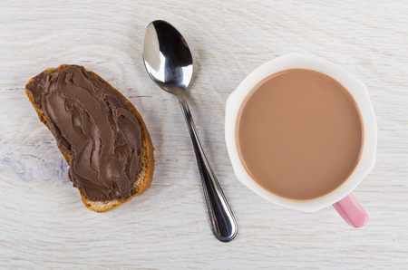 Sandwich with chocolate paste, teaspoon, cup of cocoa with milk on wooden table. Top viewの写真素材